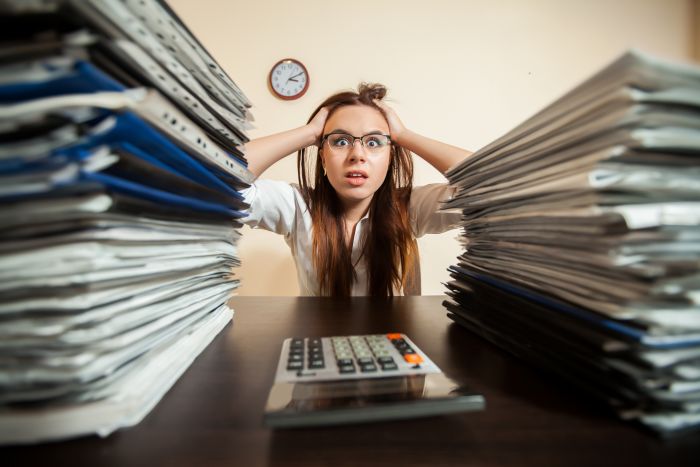 Stressed Woman Holding Her Head With Stacks Of Documents And A Calculator