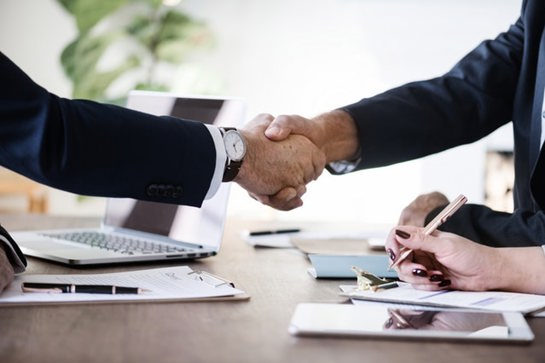 Two people shaking hands over desk with laptop and documents